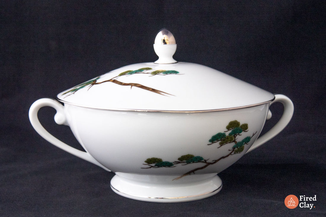 A Japanese satsuma ware soup tureen in white porcelain with hand painted trees in green brown and gold. 