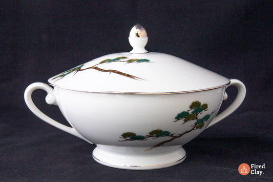 A Japanese satsuma ware soup tureen in white porcelain with hand painted trees in green brown and gold. 