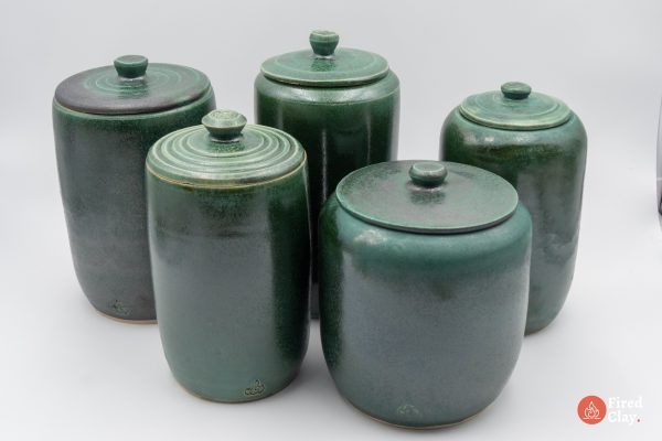 The image is of 5 tall stoneware lidded jars in a jade green glaze